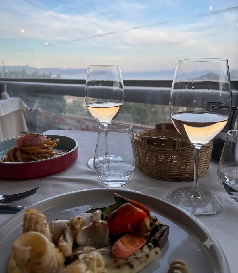 Spaghetti und gegrilltes Gemüse auf einem Terrassentisch, dazu zwei Gläser Weißwein